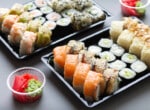 Big sushi rolls set in black plastic box for take away on gray background